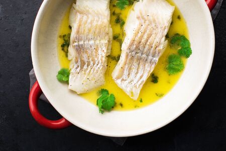 Steamed cod fillet butter-lemon sauce with herbs in the oven. Top view. In a baking dish. Healthy...