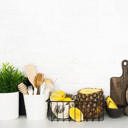 Kitchen shelf with baskets for storing products, pineapple, lemons, cutlery in a glass, chopping wooden boards on a white brick background. Style home scandi minimalism trend of modernity. Copy space,の写真素材