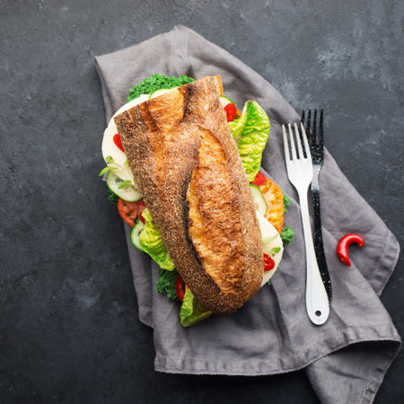 Half a baguette for a snack, lunch, dinner, sandwich with mozzarella cheese, fresh vegetables and lettuce with hot peppers on a dark background. Top view. Simple comfort food,の写真素材