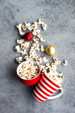 Homemade popcorn for a festive treat in red Christmas mugs with shiny New Years red and gold Christmas decorations balls. Top view. Festive atmosphere picture. Top view,の写真素材