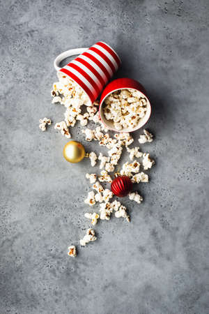 Homemade popcorn for a festive treat in red Christmas mugs with shiny New Years red and gold Christmas decorations balls. Top view. Festive atmosphere picture. Top view,の写真素材