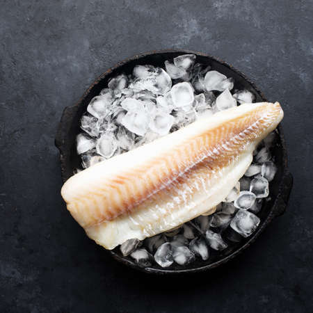 Fillet of white sea cold-water fish cod in ice cubes on a dark background. Top viewの写真素材