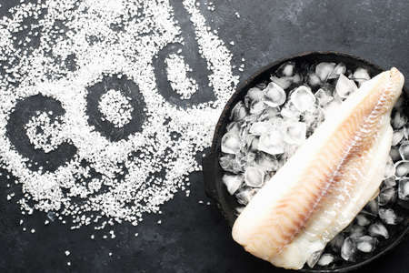 Fillet of white sea cold-water fish cod in ice cubes on a dark background. Top viewの写真素材