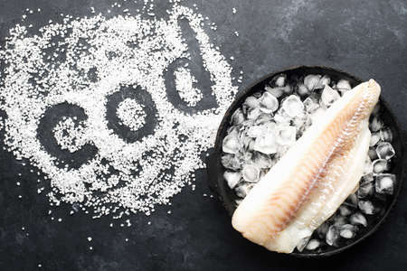 Fillet of white sea cold-water fish cod in ice cubes on a dark background. Top viewの写真素材