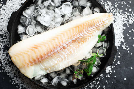 Fillet of white sea cold-water fish cod in ice cubes on a dark background. Top viewの写真素材