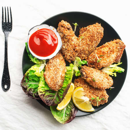 Appetizing crispy chicken wings breaded with bread crumbs with lettuce, sauce, lemon, microgreens in a plate on the table. Top viewの写真素材