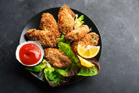 Appetizing crispy chicken wings breaded with bread crumbs with lettuce, sauce, lemon, microgreens in a plate on the table. Top viewの写真素材