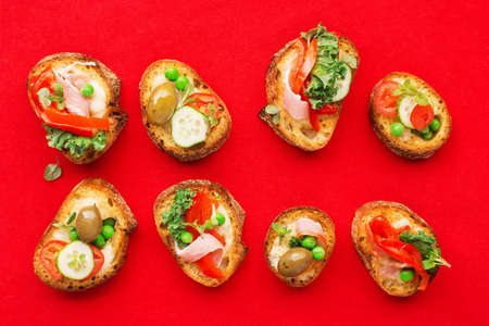 Assorted crostini canapes with cottage cheese, baked capsicum, cucumber slices, bacon, tomatoes, green peas on a festive red background. Top view,の写真素材