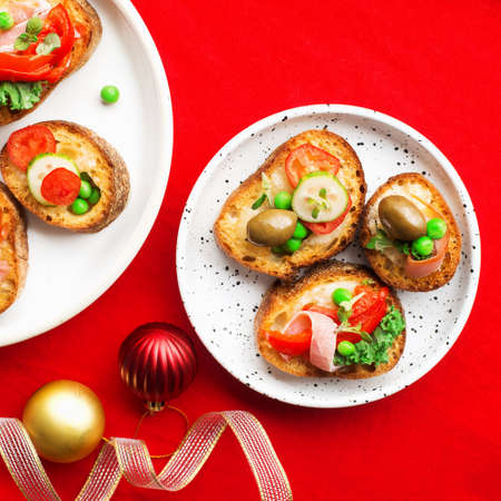 Assorted crostini canapes with cottage cheese, baked capsicum, cucumber slices, bacon, tomatoes, green peas on a festive red background. Top view,の写真素材