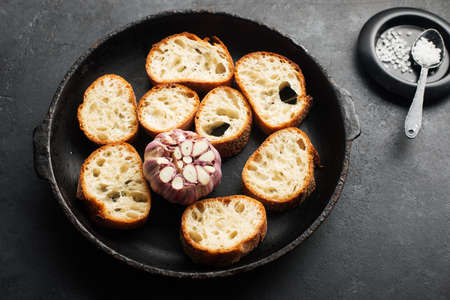 Fresh crispy crostini baguette slices with baked garlic, butter and cheese in a baking dish on a dark background. Top view. Selective focusの写真素材