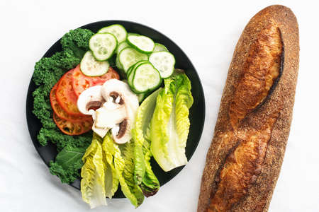Fresh baguette and vegetable slices, tomatoes, cucumber, romano lettuce leaves, mushrooms for making sandwiches for a snack. Simple homemade comfort food. Top view,の写真素材