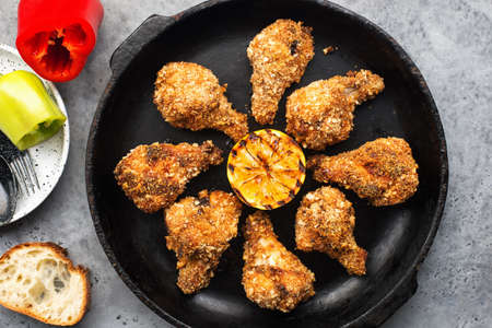 Baked chicken wings breaded with breadcrumbs in a black cast-iron pan on a dark background with grilled lemon. Top view,の写真素材