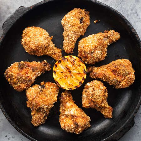 Baked chicken wings breaded with breadcrumbs in a black cast-iron pan on a dark background with grilled lemon. Top view,の写真素材