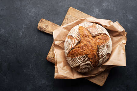 A loaf of fresh dark round buckwheat bread from a private bakery on a dark background on a vintage wooden cutting board. Top view,の写真素材
