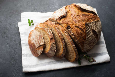 A loaf of fresh dark round buckwheat bread from a private bakery on a dark background on a vintage wooden cutting board. Top view,の写真素材
