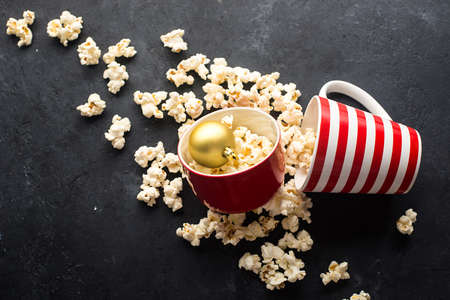 Homemade popcorn for a festive treat in red Christmas mugs with shiny New Year's red and gold Christmas decorations balls. Top view. Festive atmosphere picture. Top viewの写真素材