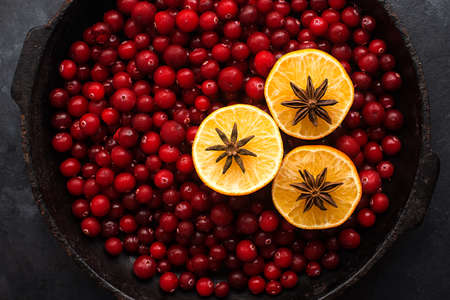 Christmas mulled wine ingredients. Lingonberry, cranberry, red berries, anise, cinnamon, orange on a dark background. Picture of a cozy home holiday. Top view.の写真素材