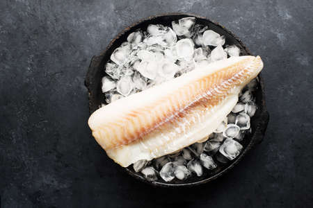 Fillet of cod fish. Saltwater white fish, raw before cooking. Healthy food ingredients. On a dark backgroundの写真素材