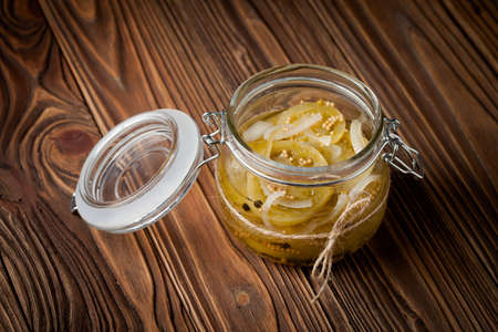 Homemade DIY natural marinated green tomatoes in a jar on wooden tableの写真素材
