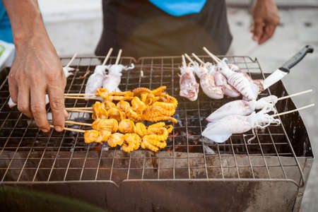 Fresh made squid barbeque skewer in hand. Traditional thai cuisine.の写真素材