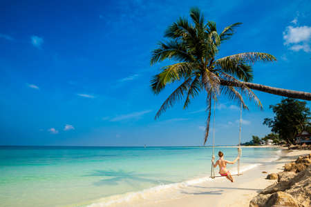 Young girl on swing on tropical island Koh Phangan in Thailand. Tourist on Chalokum beach.の写真素材
