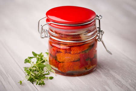 Homemade DIY natural dried red tomatoes with chilli and herbs - oregano, thyme, basil covered in oil in glass jarの写真素材