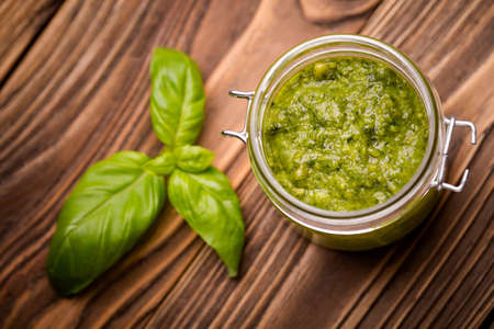 Natural homemade DIY vegan very healthy green pesto made of radish leaves and nutritional yeast flakes in a glass jar on a wooden table with basilの写真素材
