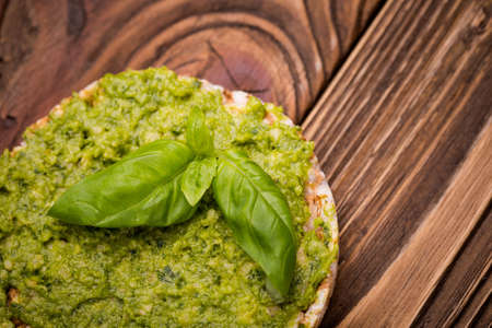 Natural homemade DIY vegan very healthy green pesto made of radish leaves and nutritional yeast flakes on a rice waffle with basil in a glass jar on a wooden tableの写真素材