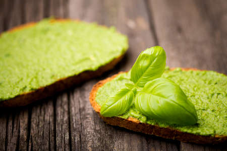 Natural homemade DIY vegan very healthy green pesto made of rocket, basil and pini nuts in a glass jar on a wooden tableの写真素材