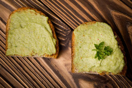 Natural homemade DIY vegan very healthy green paste made of avocado, millet gruel, chilli, garlic and parsley on bread and wooden tableの写真素材