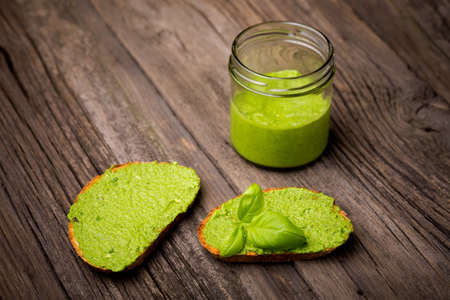 Natural homemade DIY vegan very healthy green pesto made of rocket, basil and pini nuts in a glass jar on a wooden tableの写真素材