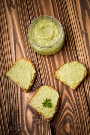 Natural homemade DIY vegan very healthy green paste made of avocado, millet gruel, chilli, garlic and parsley on bread and wooden tableの写真素材