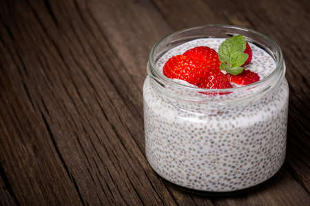 Homemade DIY natural healthy vegan dessert made from vegetable milk with rosemary and pepper, chia seeds, fresh strawberries in glass jar on a wooden tableの写真素材