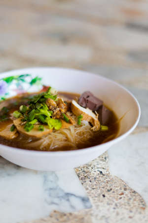 Fresh made thai dark broth noodle soup served with tofu slices, spring onion, boiled blood cubes and fried garlic. Traditional thai cuisine.の写真素材