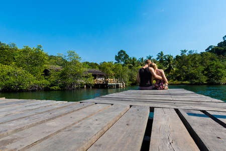 Summer landscape on tropical koh Kood island  in Thailand. Young caucasian couple sitting on pier taken from Ao Noi beach during honeymoon.の写真素材