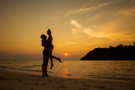 Summer landscape on tropical koh Kood island in Thailand. Young caucasian couple on white sand beach with coconut palms during colorful sunset taken on Klong Chao.の写真素材