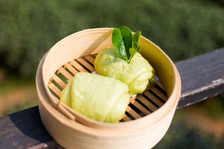 Fresh prepared asian matcha green tea buns served in bamboo steamer with tea leaf. Traditional thai sweets made of fresh ingredients.の写真素材