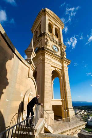 Tourist on clock tower on Church of Saint John The Baptis on Gozo island. Sacral architecture of Malta.の写真素材