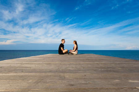 Young caucasian tourist couple seating on pier on beautiful sandy beach in Paphos. Landscape taken...