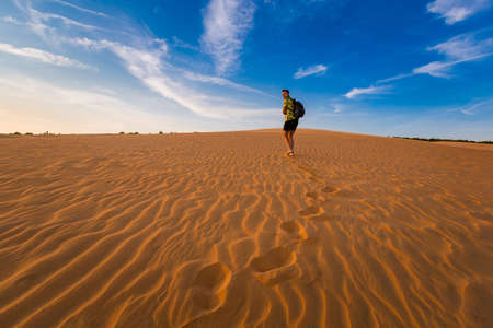 Young handsome man having fun on Red sand dunes in Mui Ne, Phan Tiet area in Vietnam. Landscape with blue sky.の写真素材