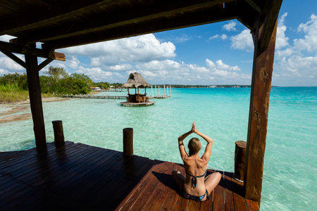 Beautiful landscape with young woman practicing yoga on a wooden pier in Laguna Bacalar in Mexico during kayak trip.の写真素材