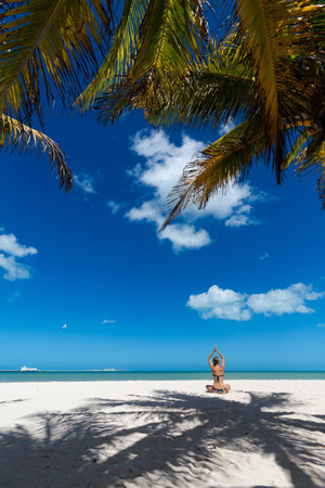Beautiful young woman meditating on a Progreso beach Mexico during a sunny day. White beach with palms and blue sky.の写真素材