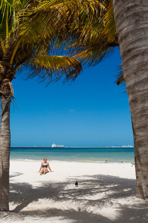 Beautiful young woman posing on a Progreso beach Mexico during a sunny day. White beach with palms and blue sky.の写真素材