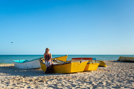 Beautiful young woman posing on a local boat in Progreso beach Mexico during sunny day. White beach and blue sky.の写真素材