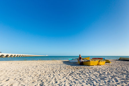 Beautiful young woman posing on a local boat in Progreso beach Mexico during sunny day. White beach and blue sky.の写真素材
