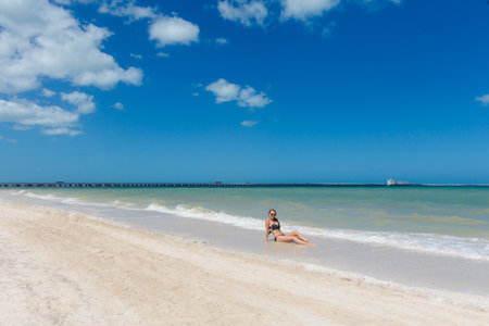 Beautiful young woman posing on a Progreso beach Mexico during a sunny day. White beach with palms and blue sky.の写真素材