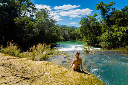 Young pretty woman relaxing by the water in Roberto Barrios cascadas park, Palenque in Mexico. Vivid landscape photo with lush green and crystal water during sunny day.の写真素材
