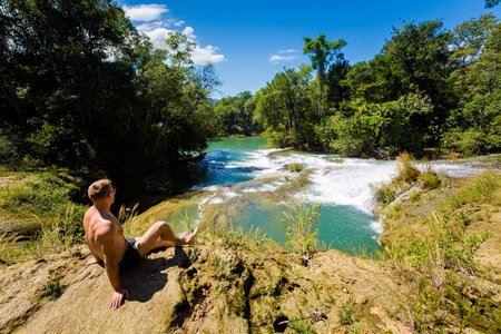 Young handsome man in Roberto Barrios cascadas park, Palenque in Mexico. Vivid landscape photo with lush green and crystal water during sunny day.の写真素材