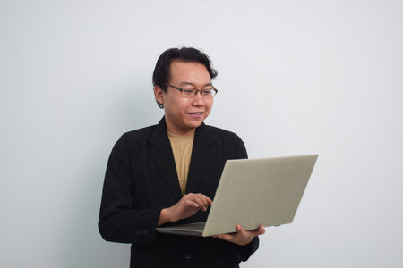 Happy asian businessman reading or typing project with laptop in isolated white backgroundの写真素材