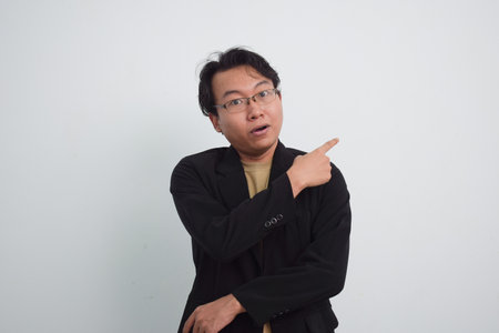 Joyful asian businessman with suit and casual shirt showing product or pointing gesture in isolated...